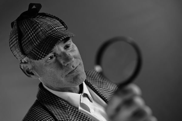 Man with checkered hat and magnifying glass thinking about using an AI Essay Checker